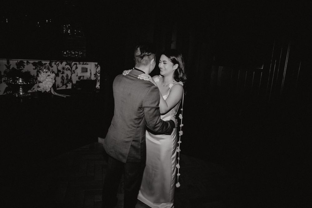 A couple shares a romantic slow dance together at a dimly lit reception venue in black and white.