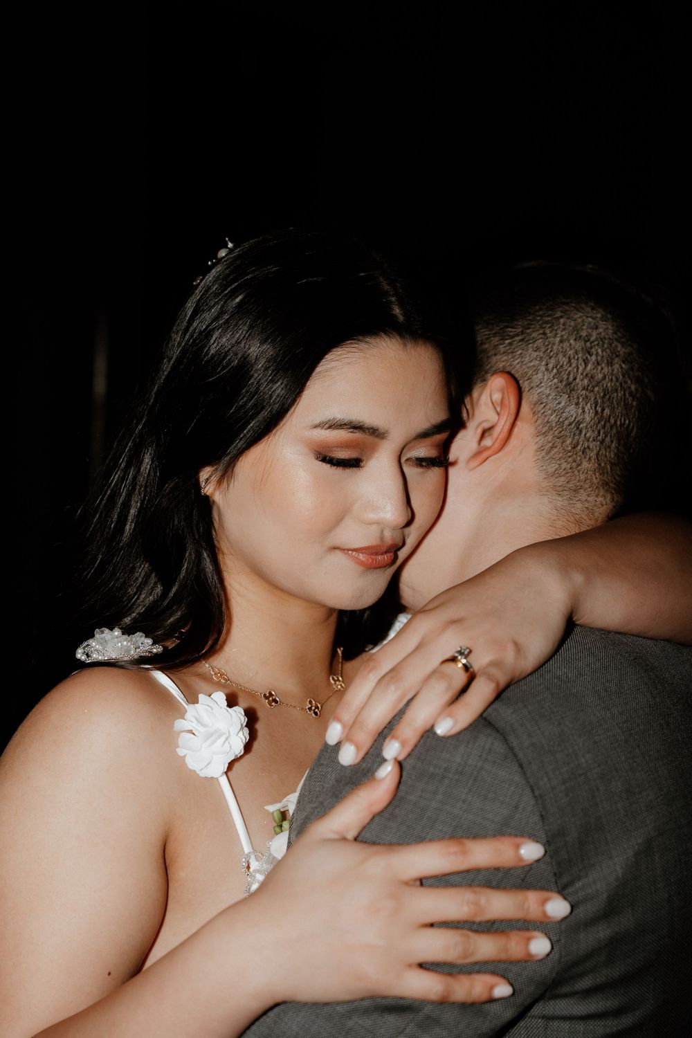A tender moment between newlyweds with the bride in white showing her ring while embracing her partner.