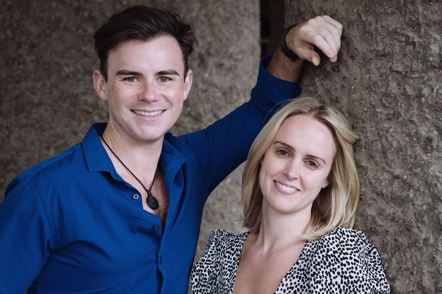 Man and woman standing next to each other while the man rests his arm against a wall
