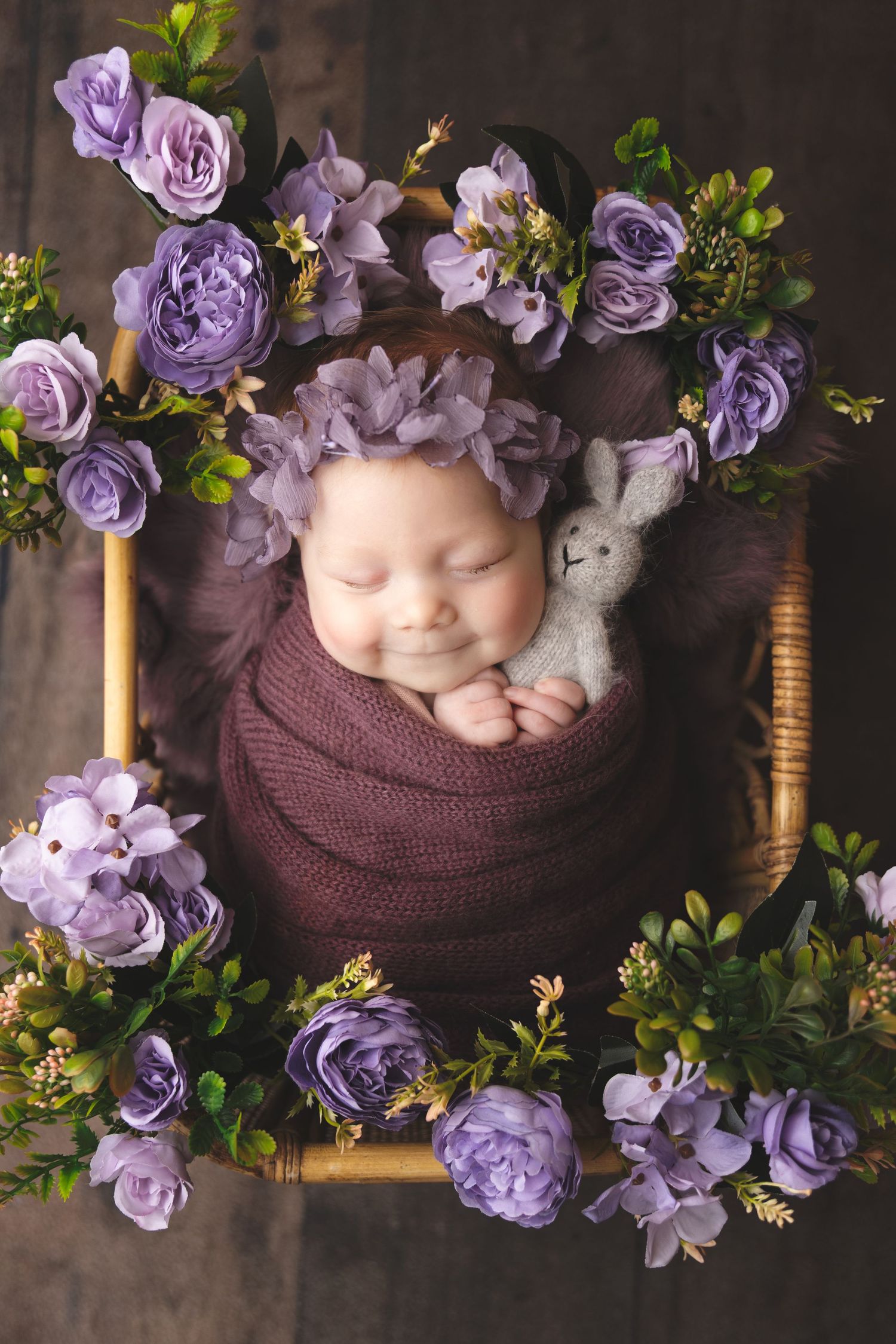 newborn photography session Sammamish WA with purple floral decorations and brown wrap on wooden backdrop.