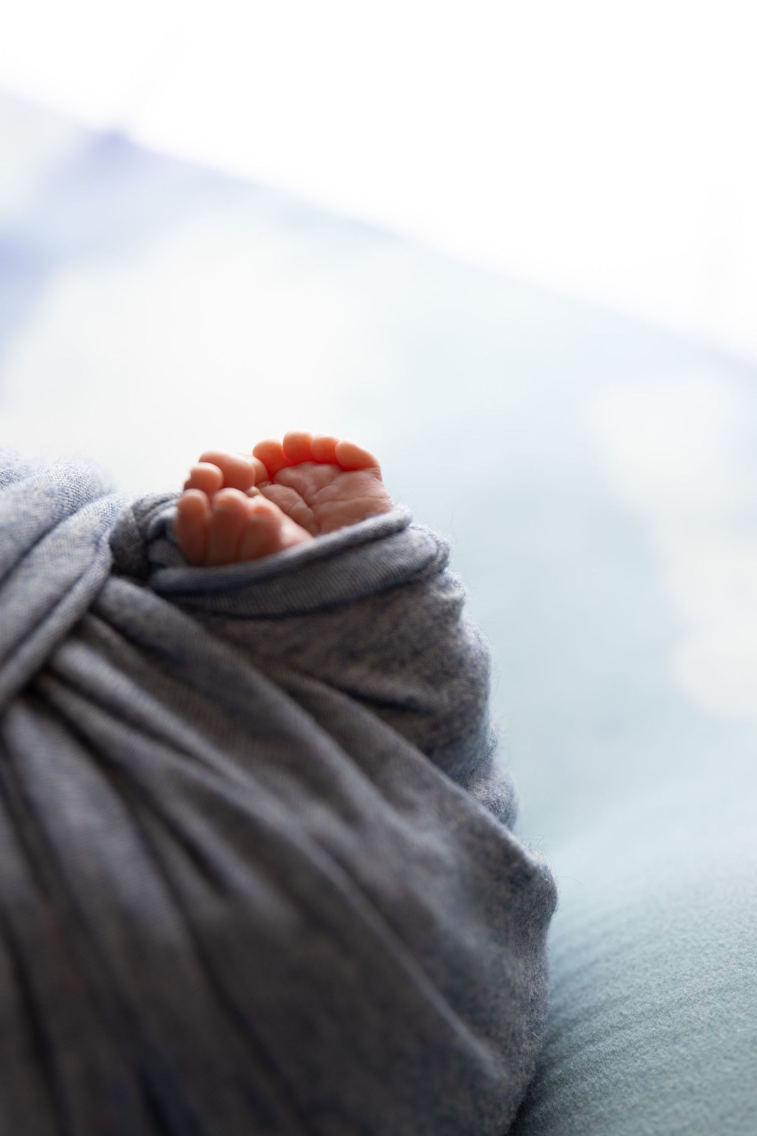 newborn photography session Sammamish WA, Tiny newborn baby toes peek out from soft gray swaddling blanket in gentle lighting.