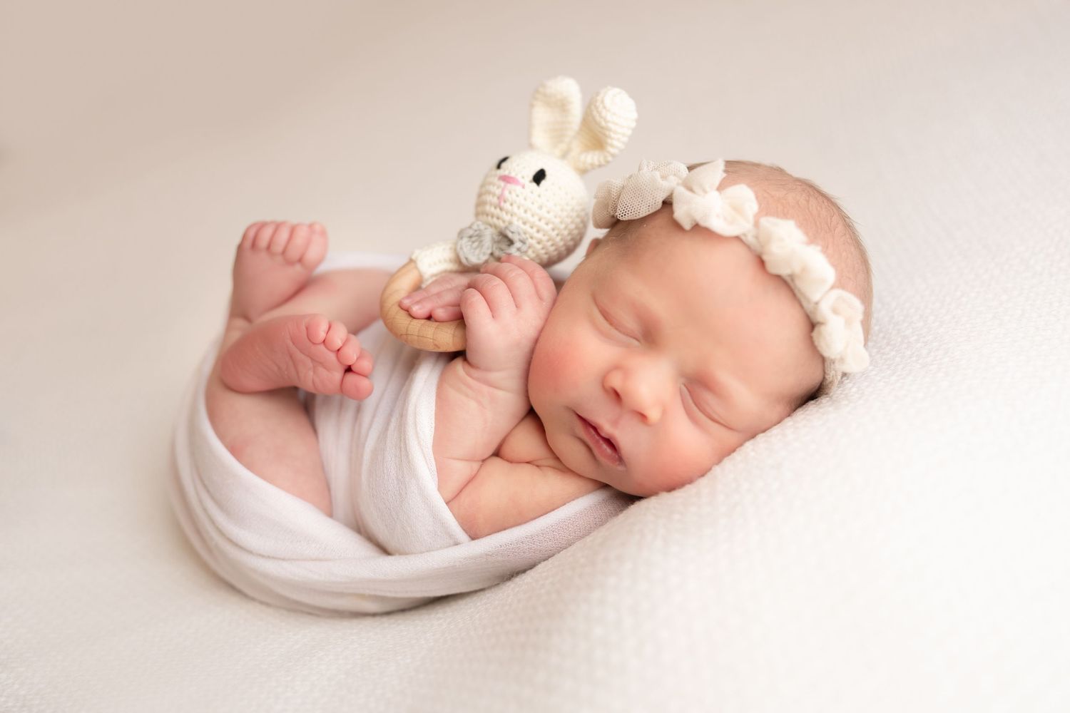 newborn photography session Sammamish WA in white wrap cuddling small plush mouse toy on cream backdrop.