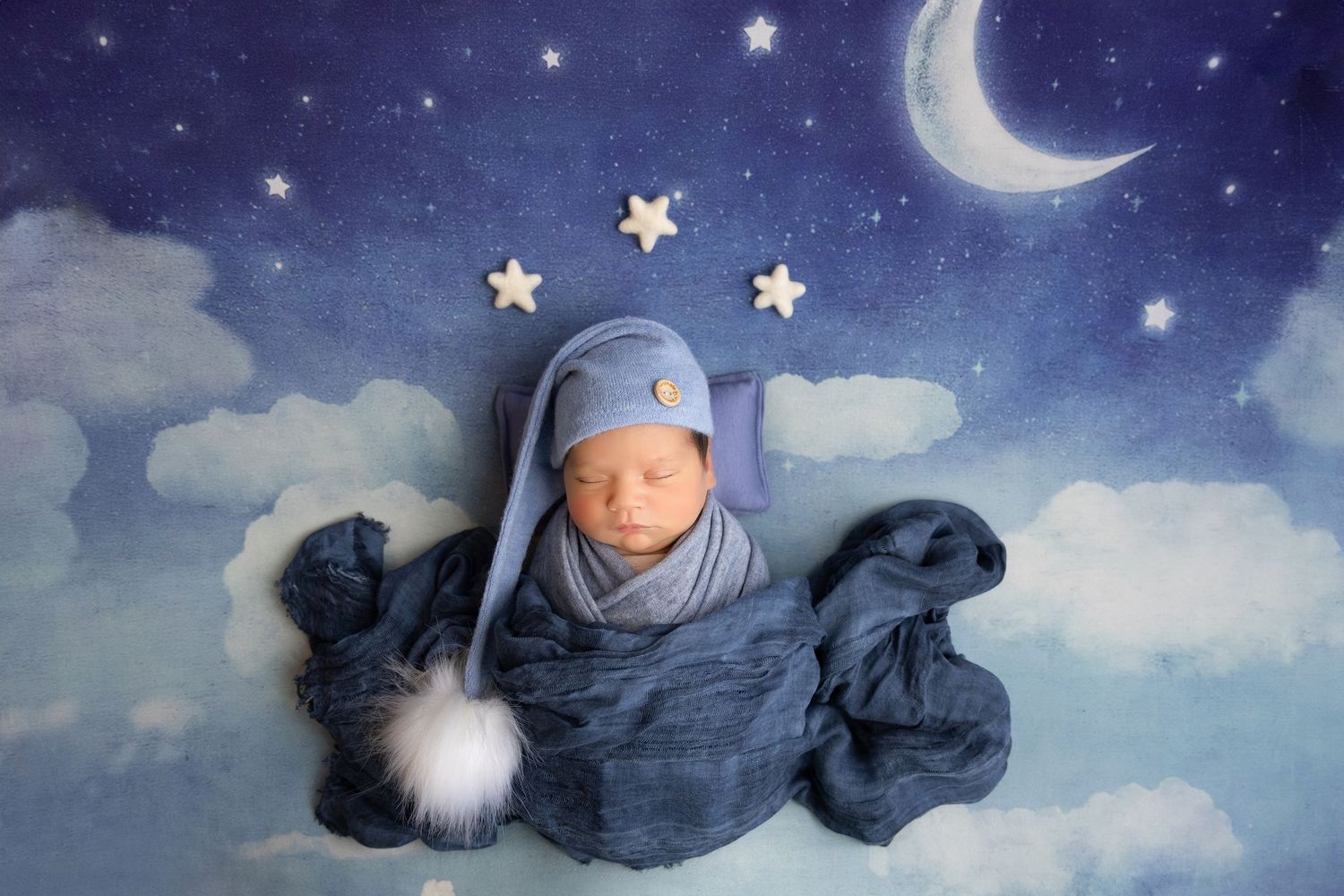 newborn photography session Sammamish WAswaddled in blue fabric lies on a dreamy nighttime backdrop with clouds, moon and stars.
