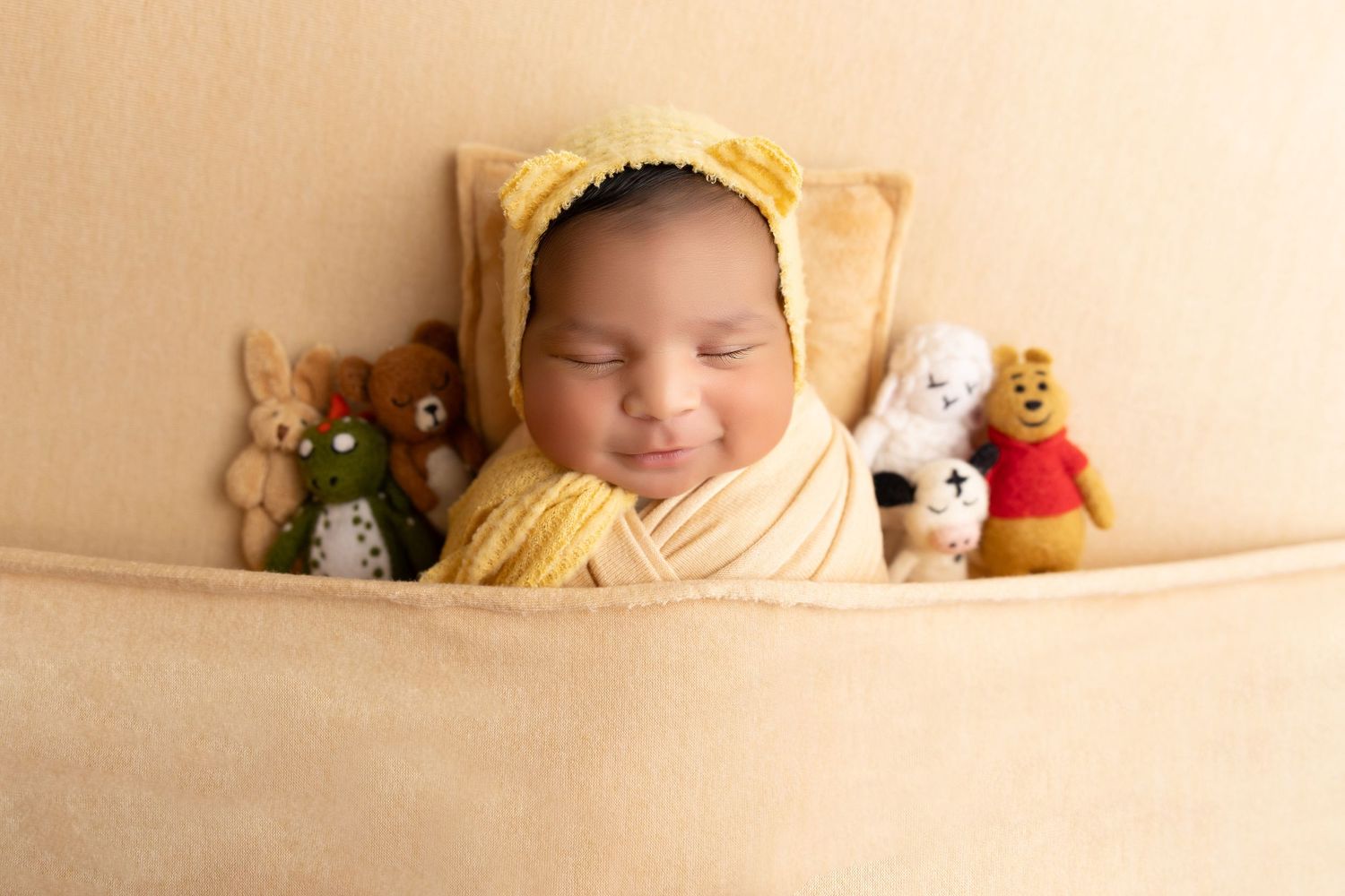 newborn photography session Sammamish WA in yellow fabric rests peacefully surrounded by plush stuffed animal toys on a beige background.