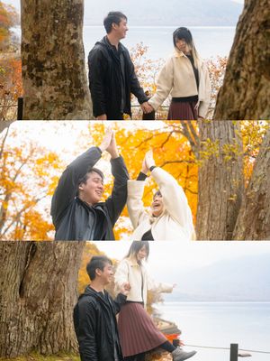 A joyful couple laughs and plays together among golden autumn trees beside a serene lake.