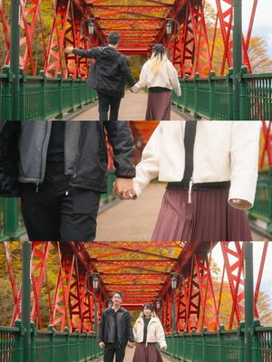 A couple walks hand in hand across a vibrant red iron bridge surrounded by autumn foliage.