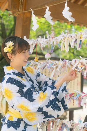 Young woman in a floral blue and yellow yukata kimono touching colorful charms at a Japanese shrine.