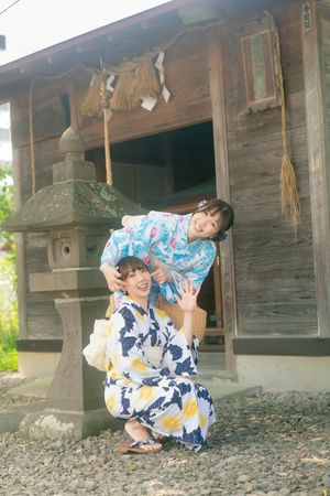 Two young women in matching floral yukatas posing playfully outside a traditional Japanese shrine.