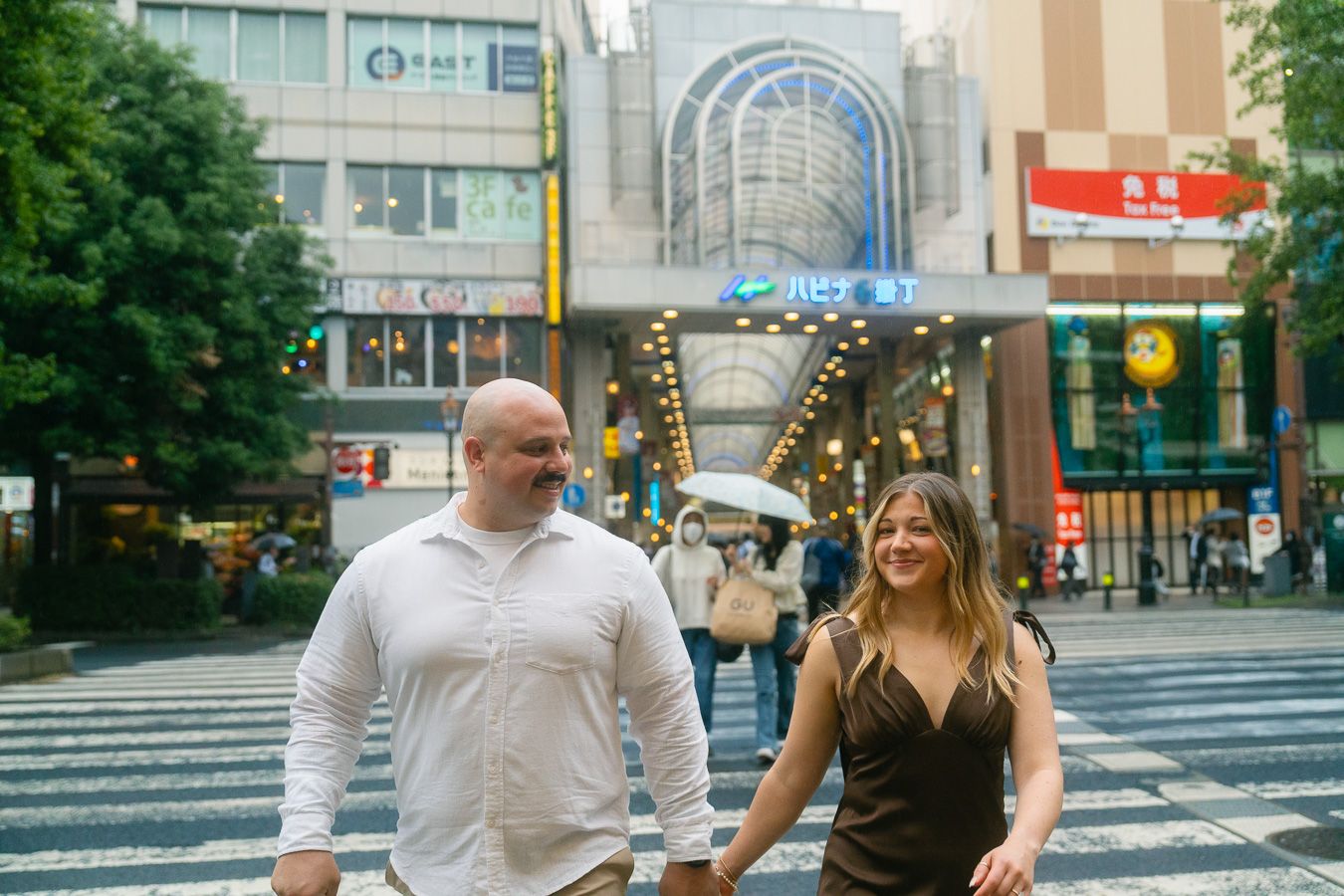 Couple holding hands crossing a busy street in Japan with colorful city signs and buildings in the background.