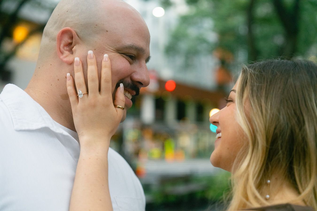 Happy couple sharing a joyful moment outdoors, woman showing engagement ring while smiling at her partner.