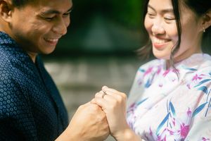 Smiling couple in traditional Japanese attire sharing a tender moment while looking at an engagement ring together outdoors.