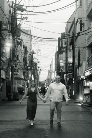 Couple holding hands walking down a bustling urban street in black and white photo.