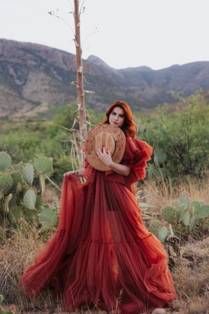 Flowing red tulle dress photographed against desert mountains and cacti in dramatic outdoor fashion shoot.
