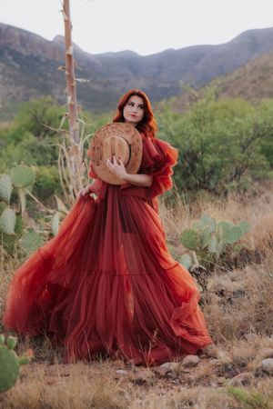 Dramatic red gown billows in desert landscape with mountains and cacti in background.