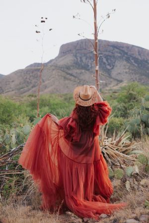 Western-inspired fashion shoot features flowing red dress and hat in desert setting.