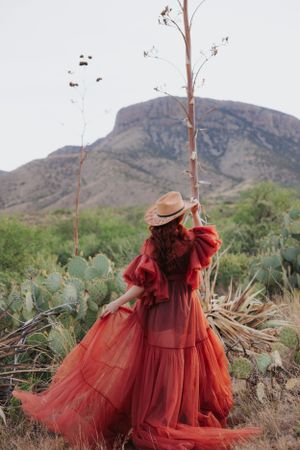Desert fashion photography featuring dramatic red dress and straw hat against mountain scenery.