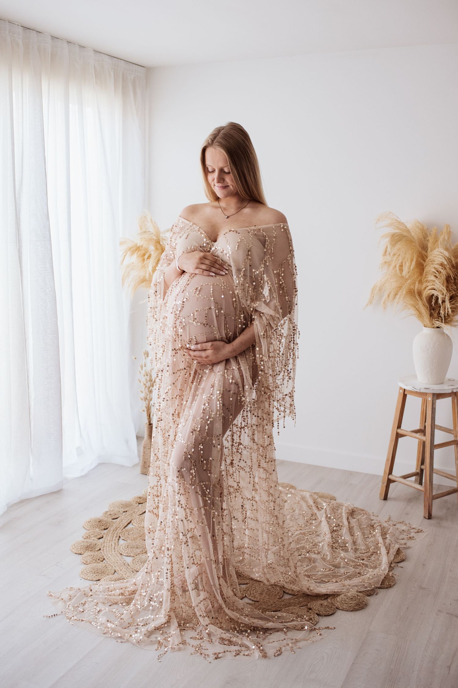 A maternity photo featuring an elegant champagne-colored lace gown with a flowing train against a white backdrop.