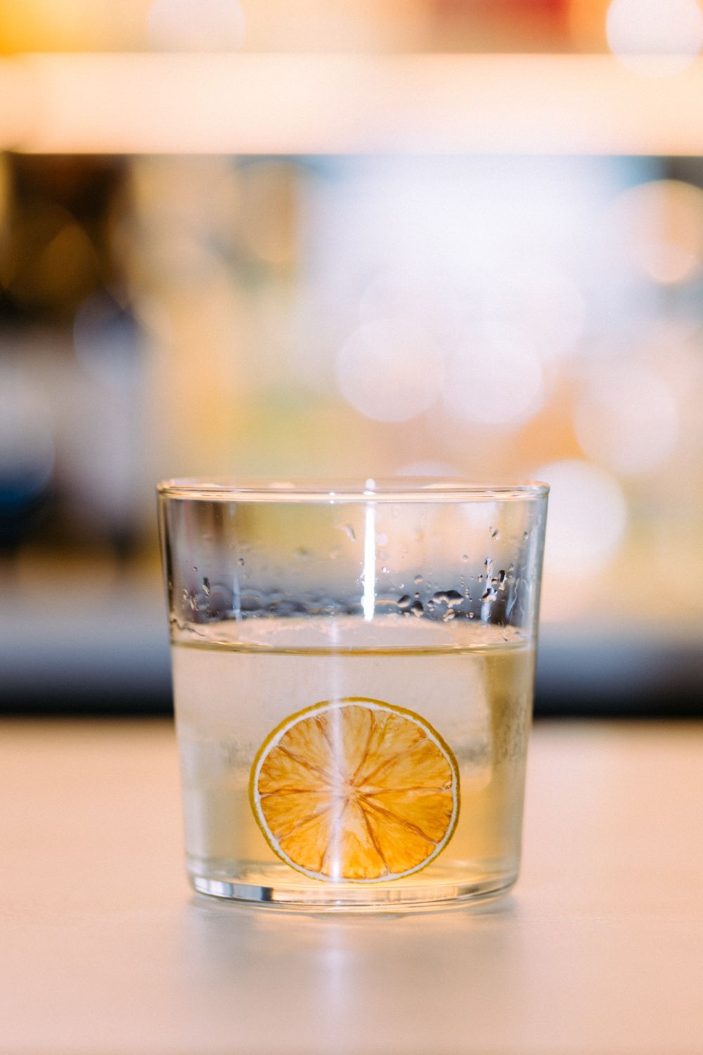 A clear cocktail glass with a floating lemon slice and bubbles in a soft-focused setting.