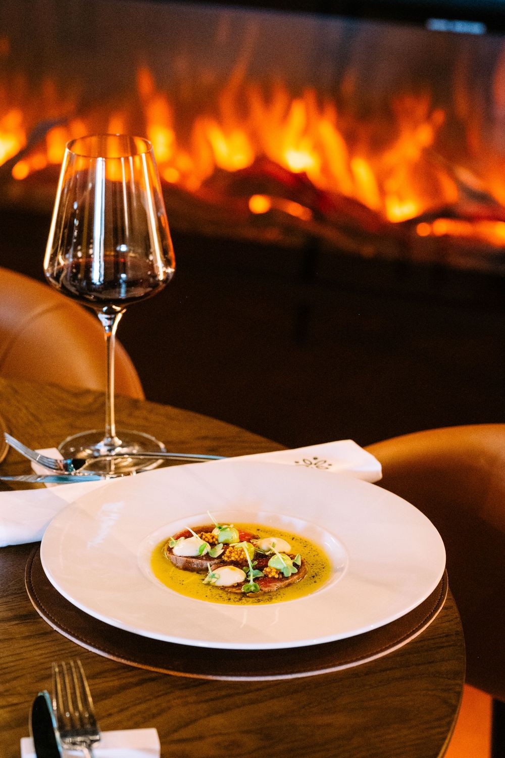 Elegant plated soup dish and wine glass on wooden table with warm fireplace flames glowing in the background.