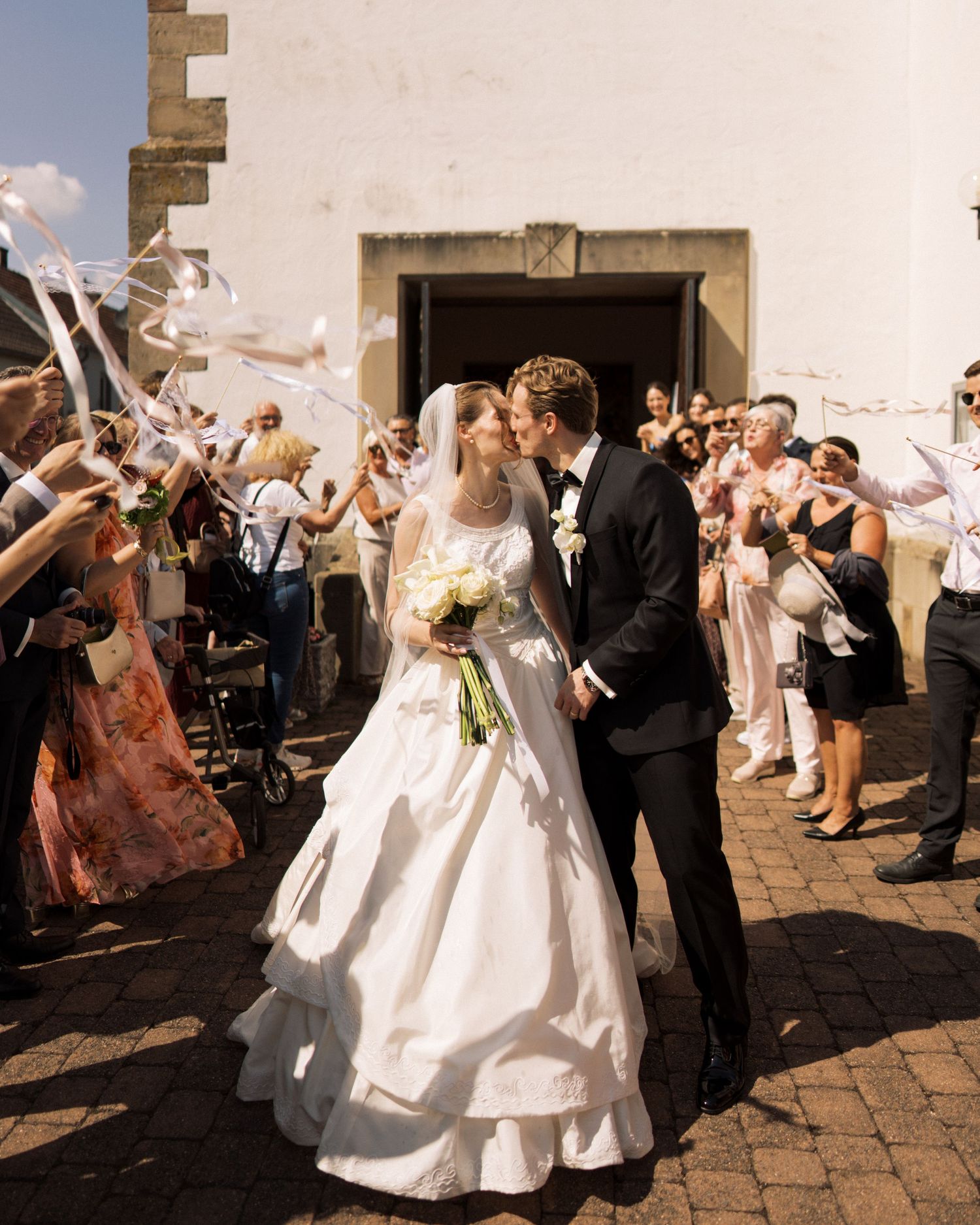 Elegant couples in white attire stroll along a scenic outdoor walkway.