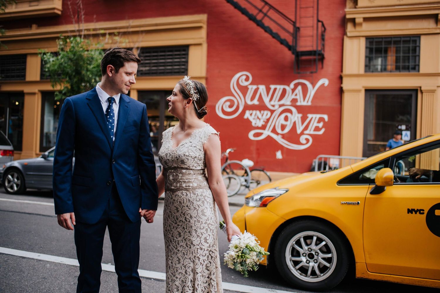 Couple walking past yellow taxi cab on city street with vintage signage.