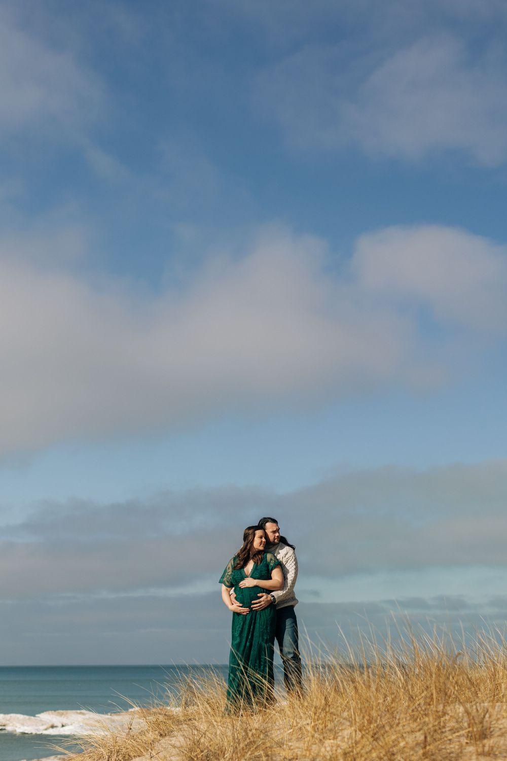 Intimate beach portrait of a couple standing in tall grass against a blue sky background.