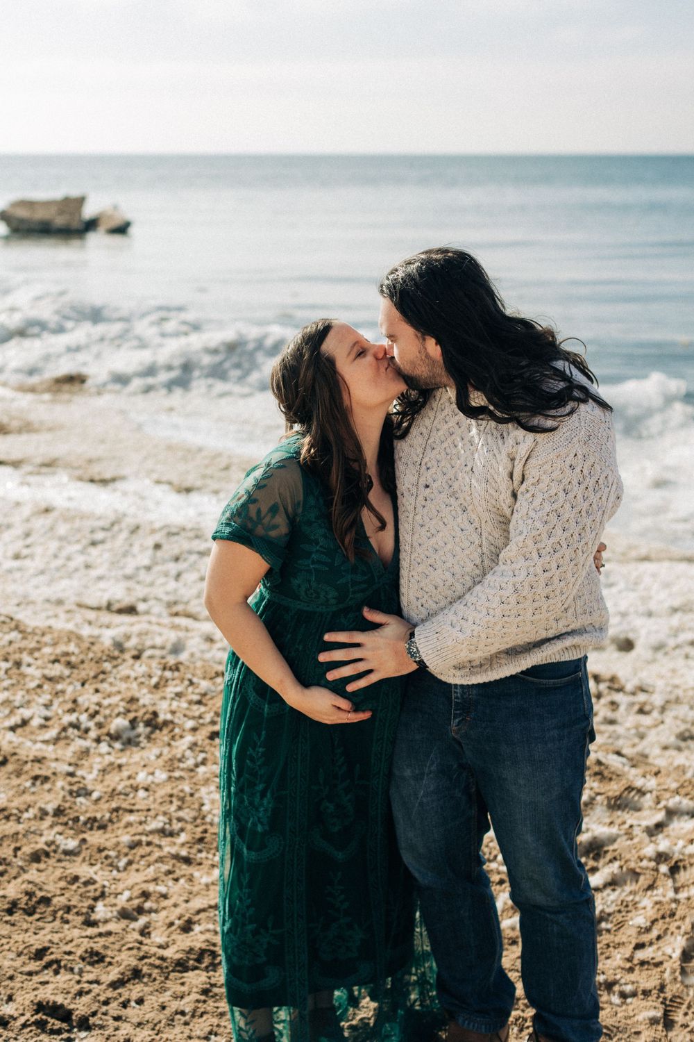 An intimate moment between a couple on a rocky beach with waves in the background.