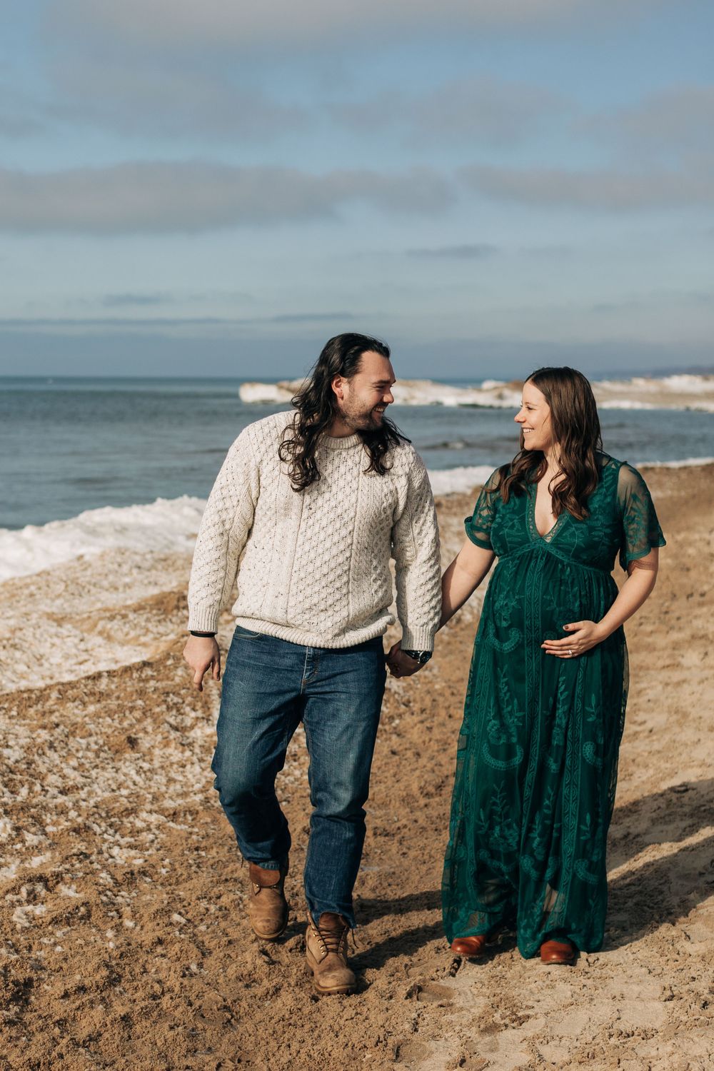 A couple walks along a beach shoreline wearing casual winter attire.