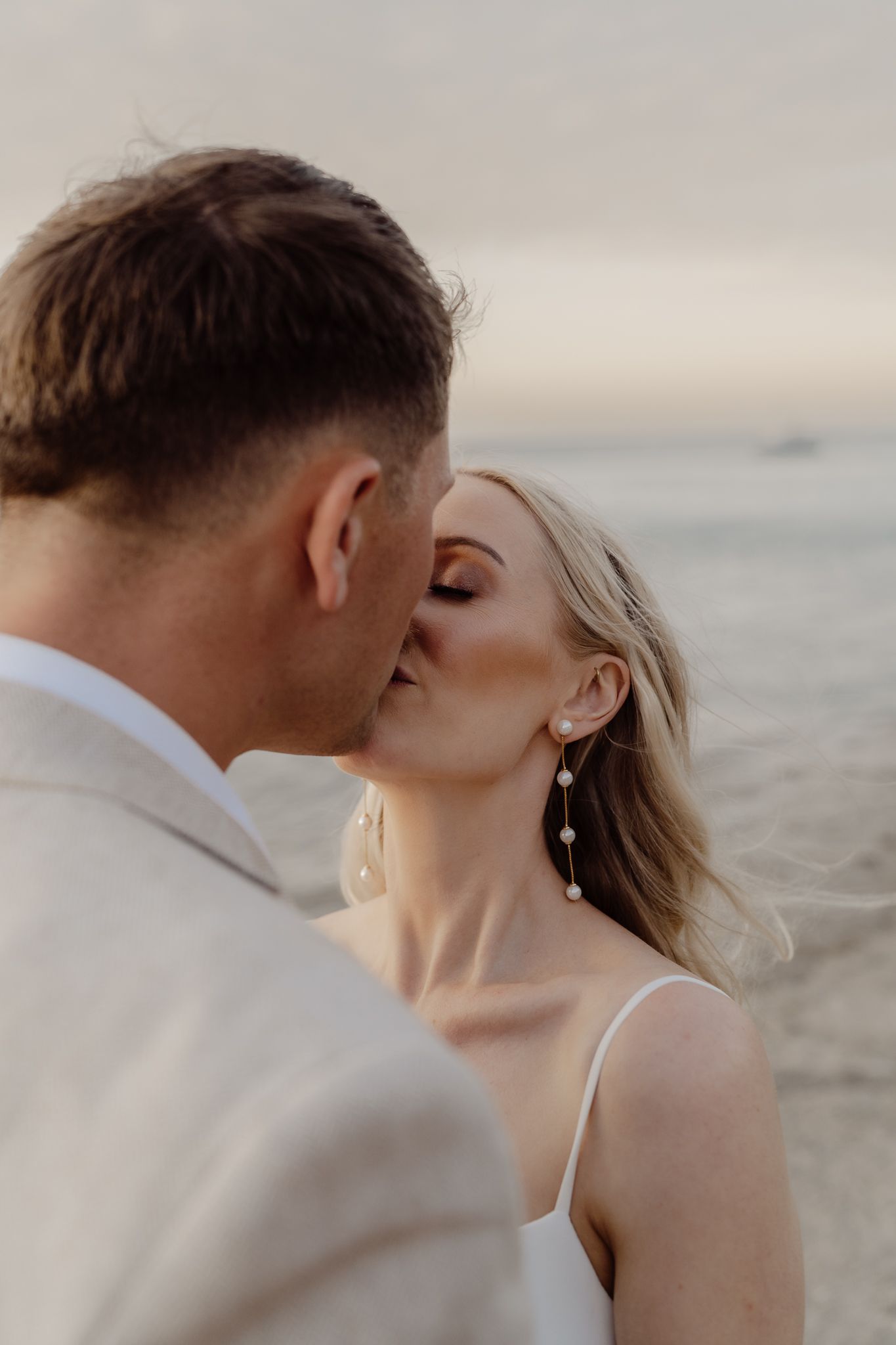 Newly married couple kissing at golden hour with the ocean behind them