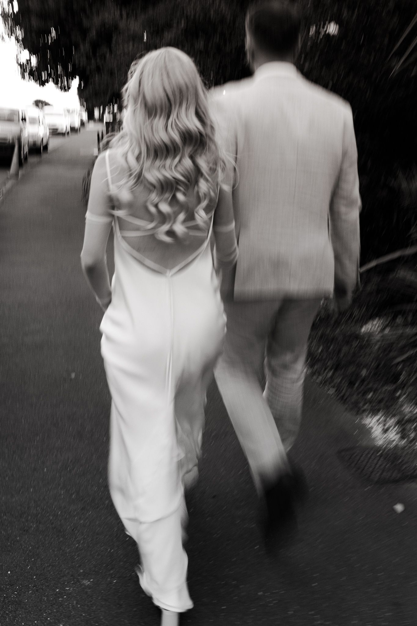 A black and white wedding photo of a couple walking away from the camera down a street