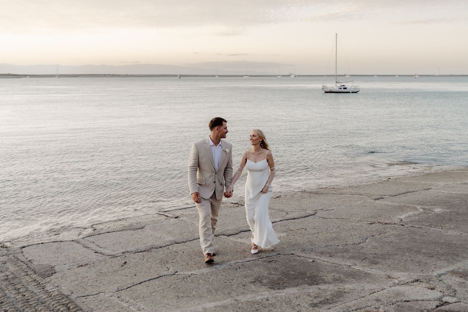 A natural wedding photo of a couple walking toward the camera as the sun sets behind them