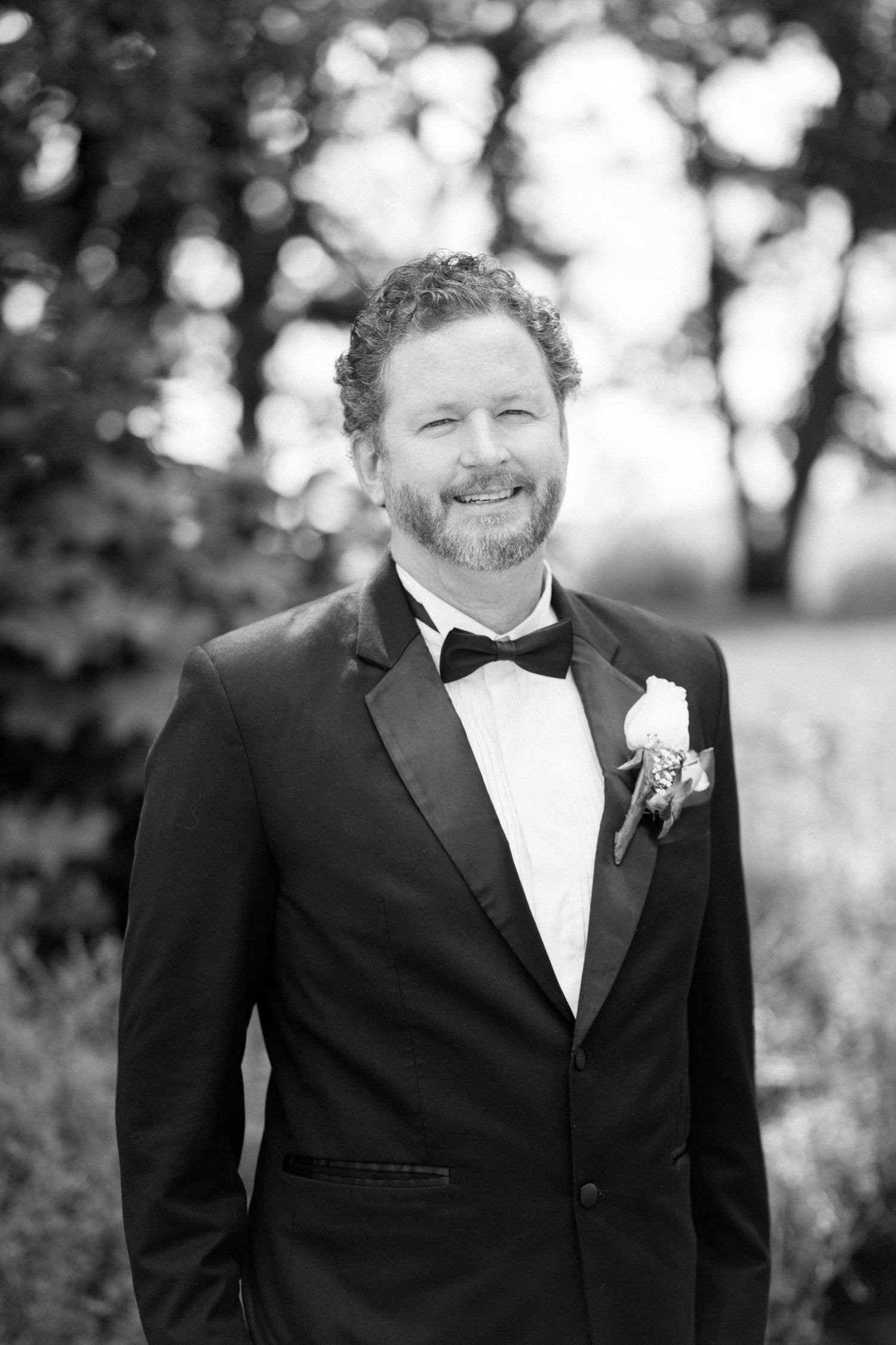 Portrait of groom in black tuxedo and bow tie outdoors with bokeh background.