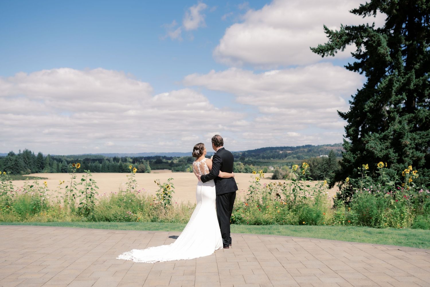 Wedding couple stands on outdoor patio overlooking scenic mountain valley landscape.