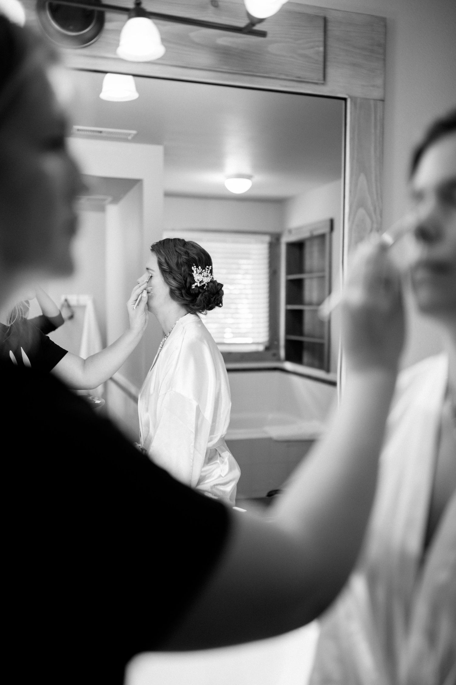 Black and white photo of bridal preparation with reflection in dressing room mirror.