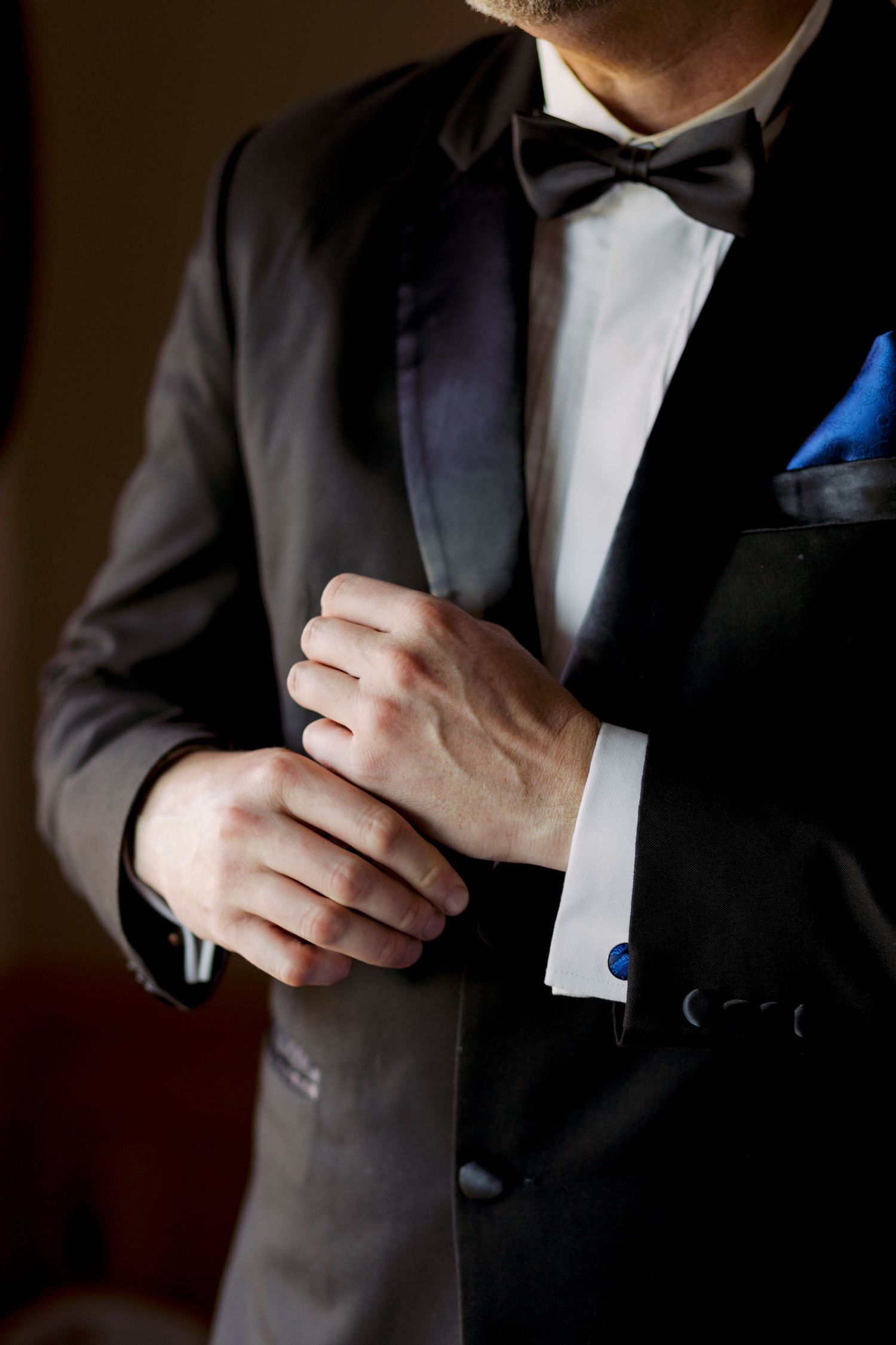 Close-up of hands adjusting cufflinks on a formal black tuxedo with bow tie.
