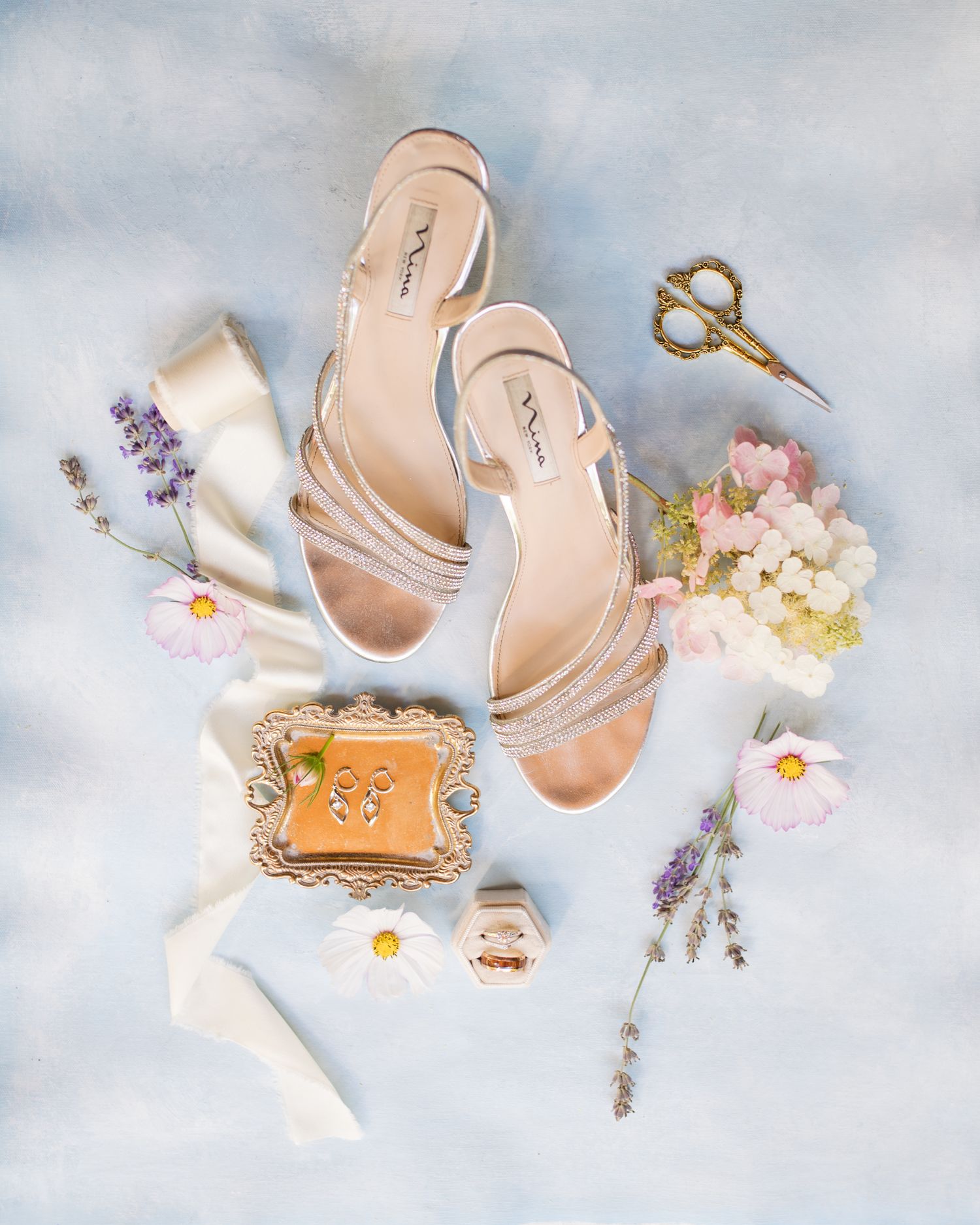 Elegant nude wedding heels with floral accents and vintage scissors on light blue background.