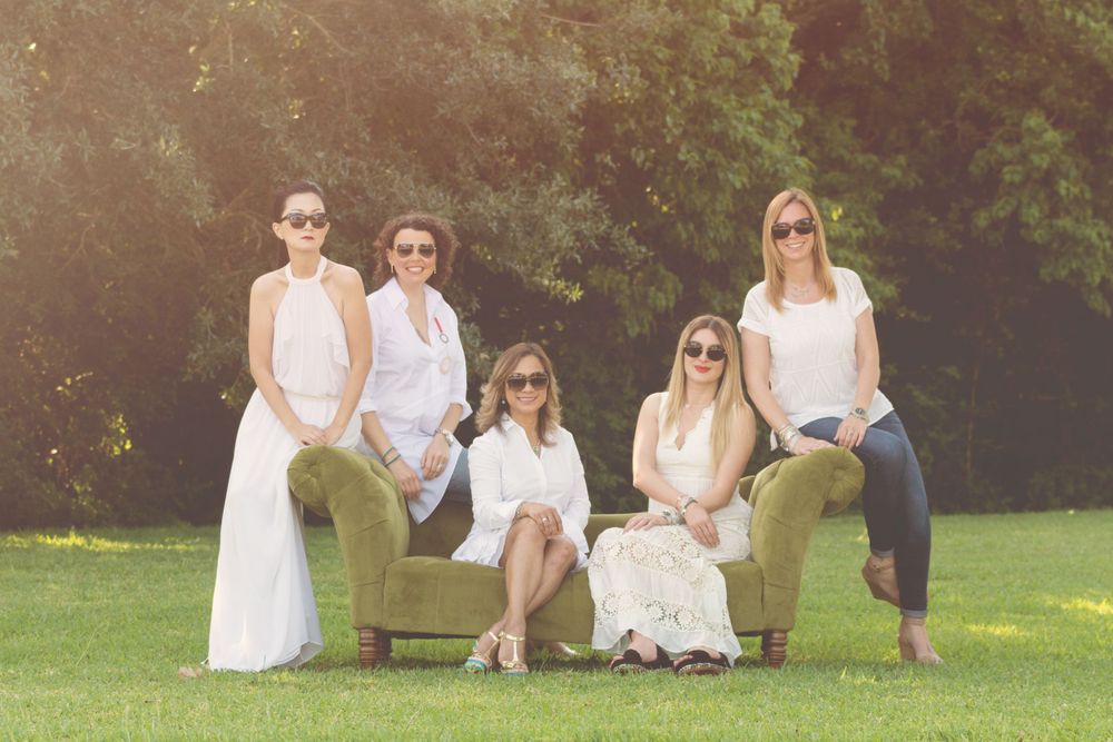 5 adult female friends sitting on a couch in a field while wearing sunglasses