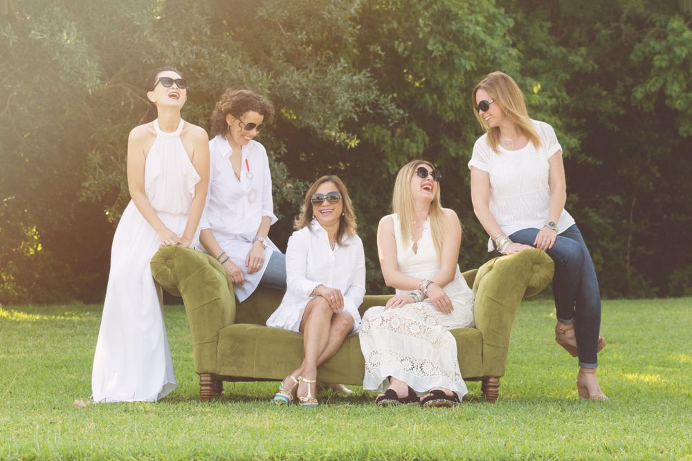 5 adult female friends sitting on a couch in a field while wearing sunglasses