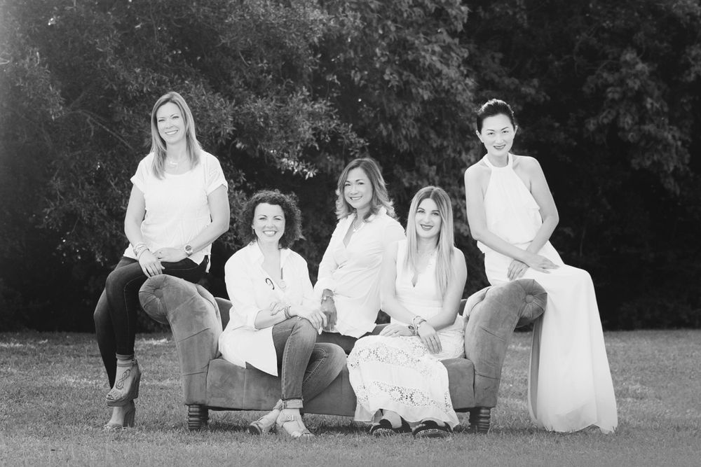black and white 5 adult female friends looking and laughing at each other on a green couch in a field