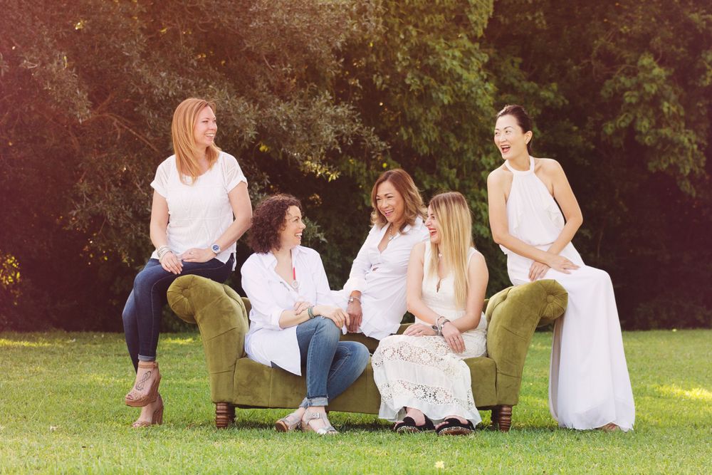 5 adult female friends looking and laughing at each other on a green couch in a field
