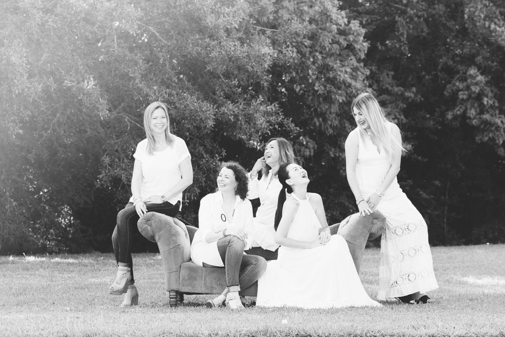 black and white 5 adult female friends looking and laughing at each other on a green couch in a field