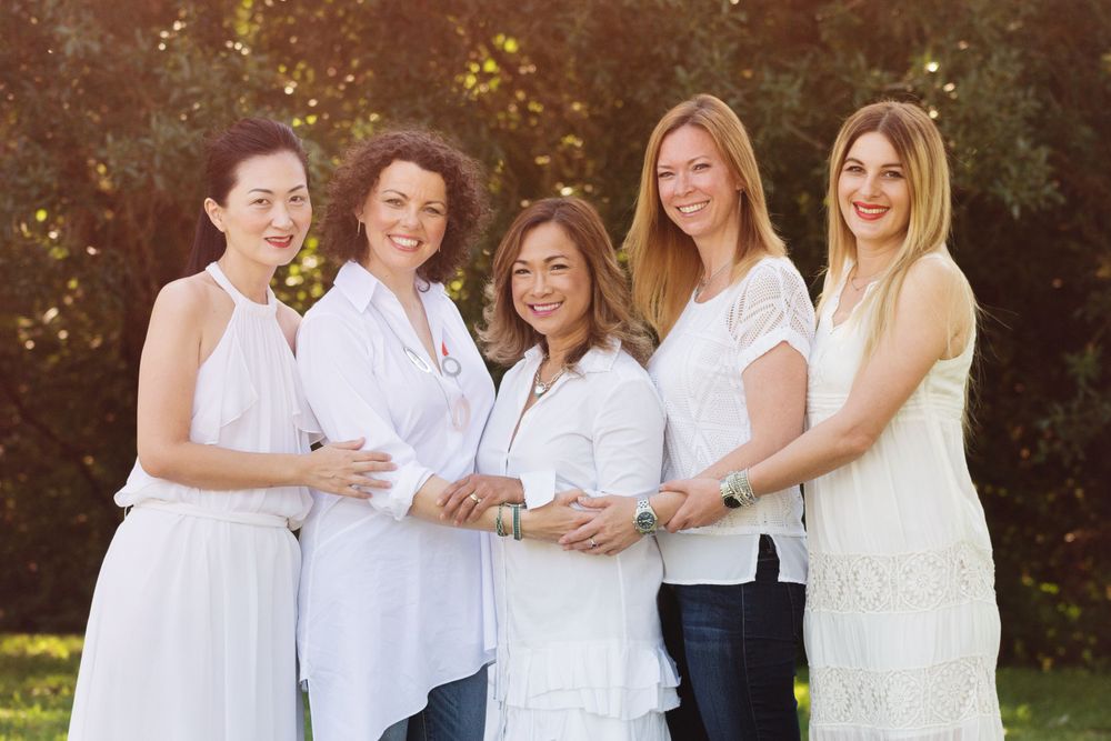 5 women standing together all wearing white