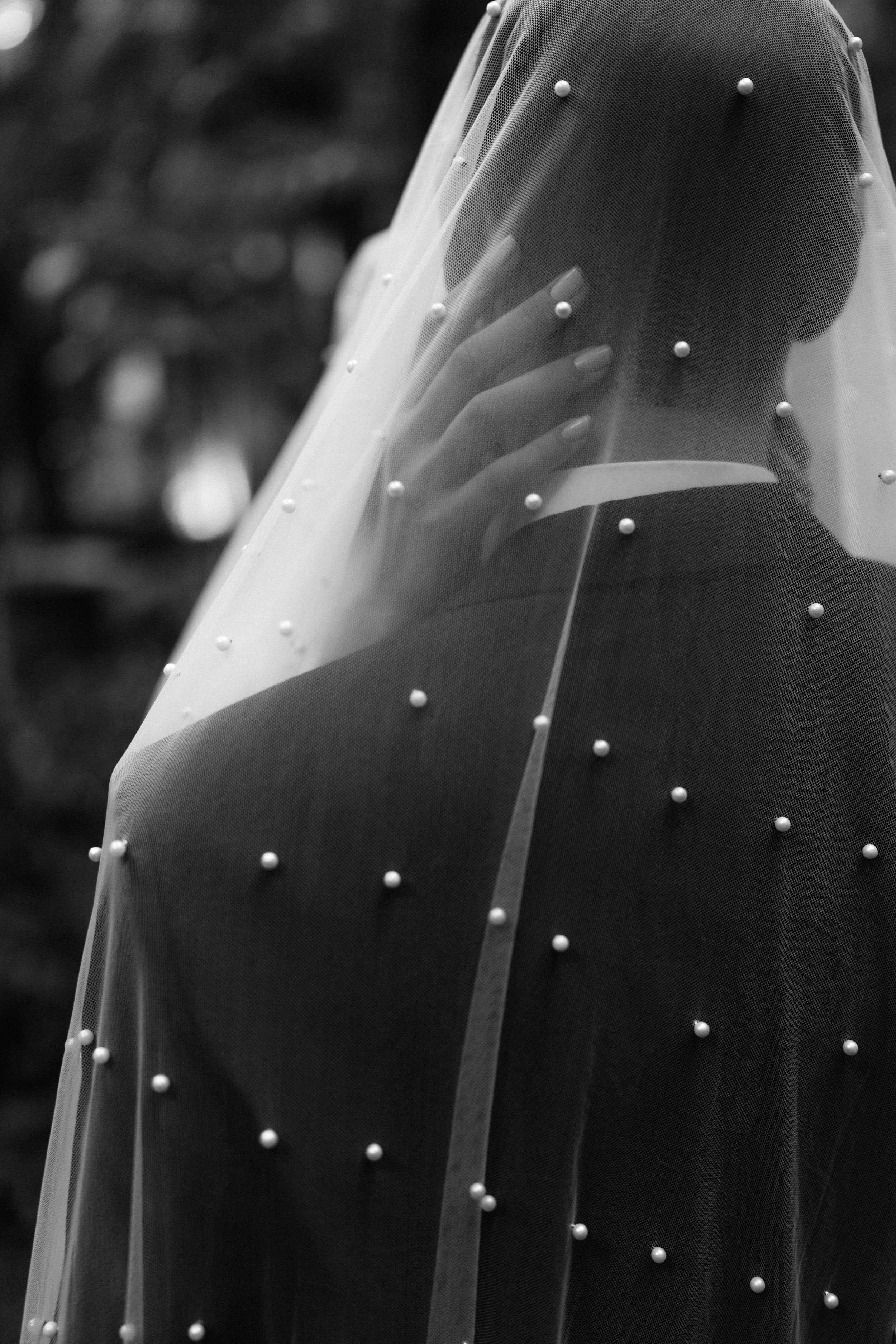 A bridal veil adorned with scattered pearl embellishments is photographed in elegant black and white.