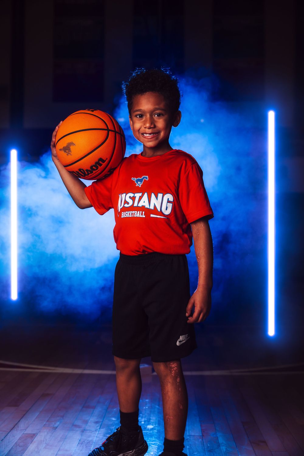 Basketball player poses with orange ball against dramatic blue lighting and smoke effects.