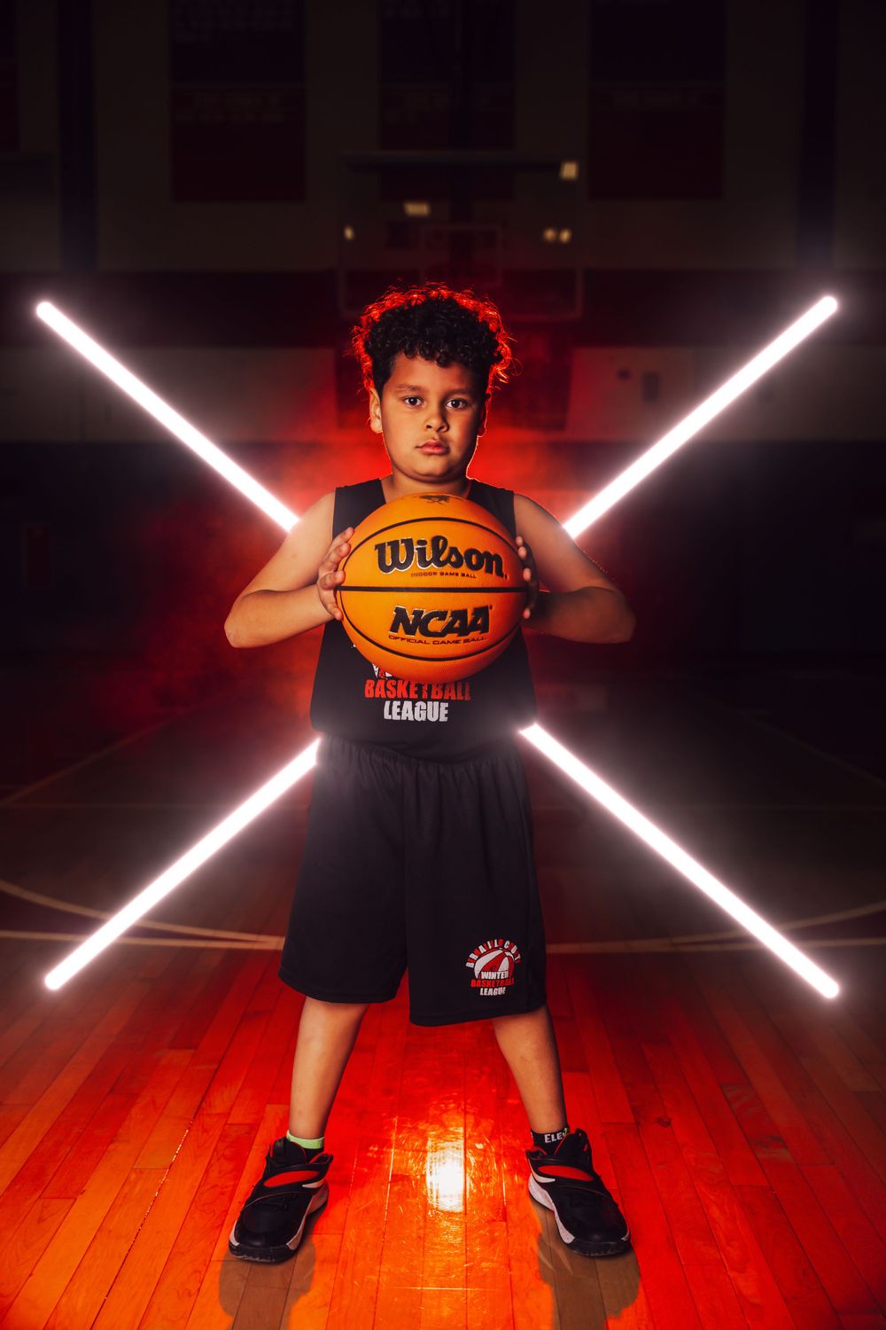Dramatic sports photo shoot with basketball against red lighting and crossed LED light bars on wooden court.