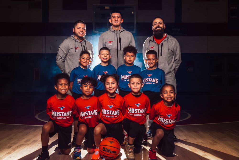 Youth basketball team poses with coaches on indoor court.