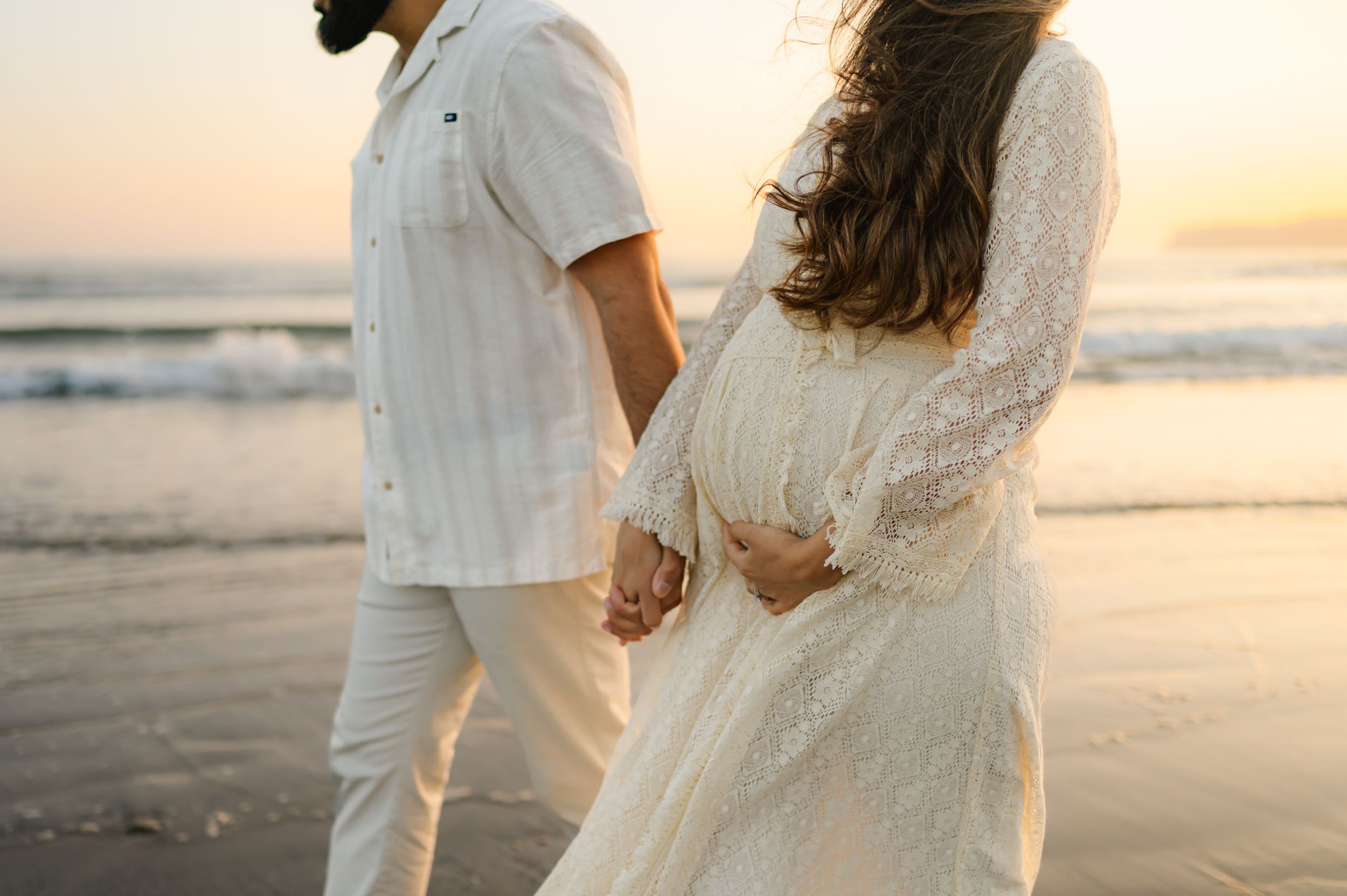 A couple holding hands on the beach at sunset during Ventura beach photoshoot by Ventura maternity photographer
