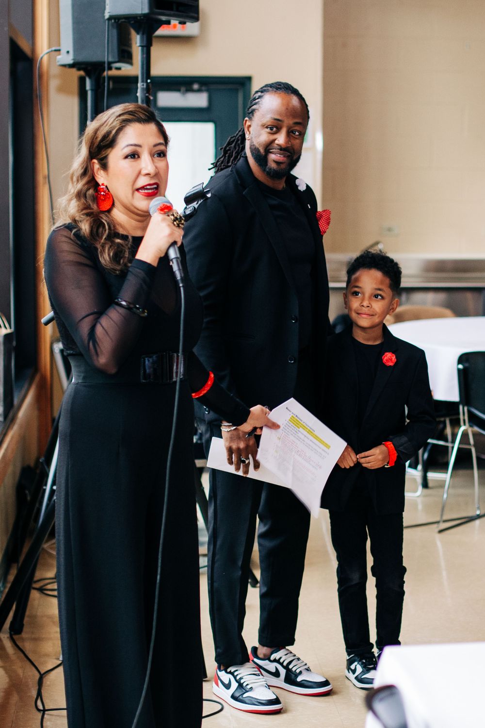 Three performers with microphones stand together on stage wearing formal attire.