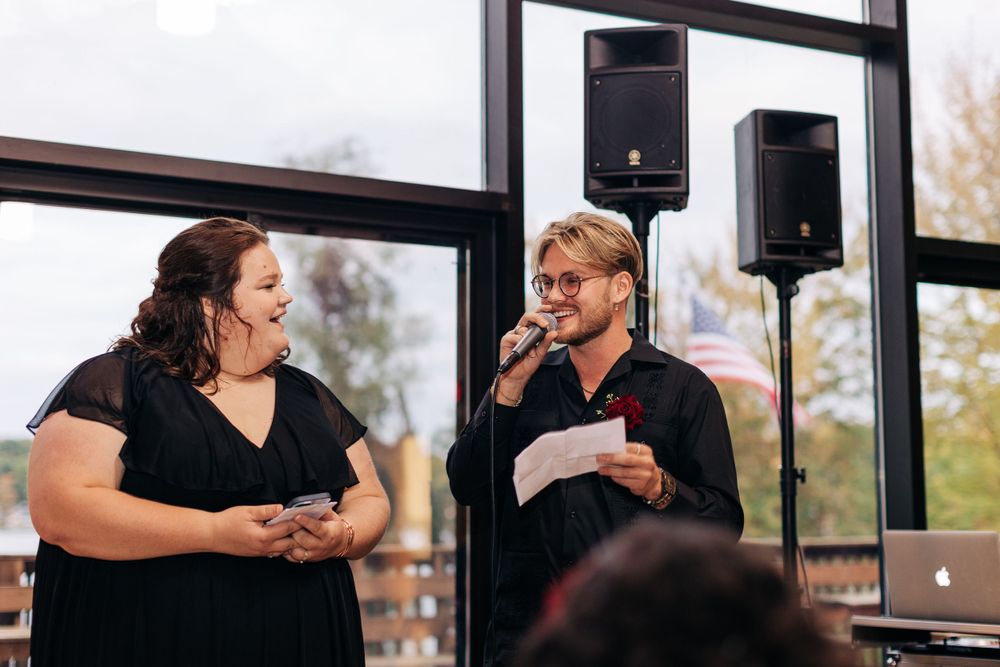 Two people sharing a lively conversation while presenting at an indoor event with speakers in the background.