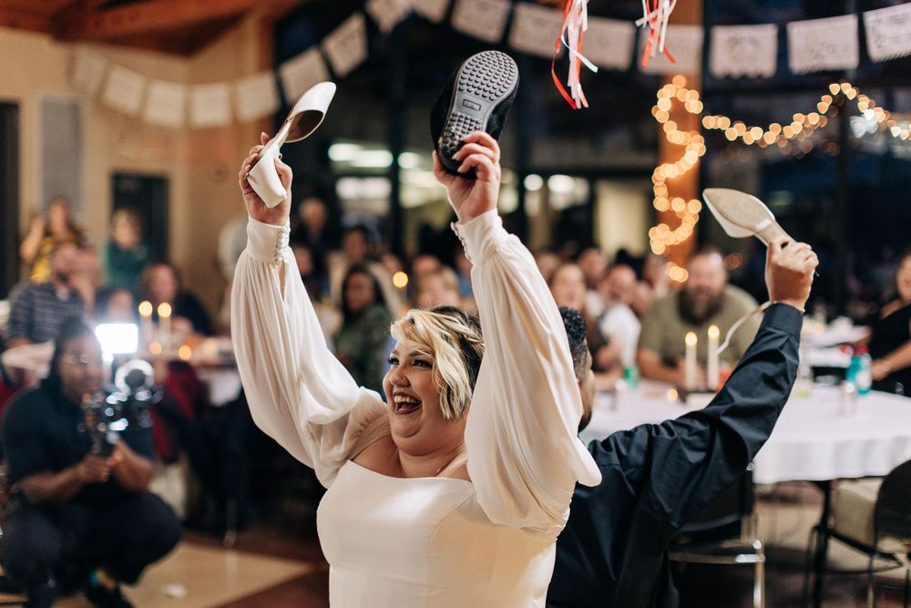 A person in a white dress celebrates joyfully with raised arms during a wedding reception.